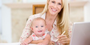 Mother and baby in dining room with laptop smiling